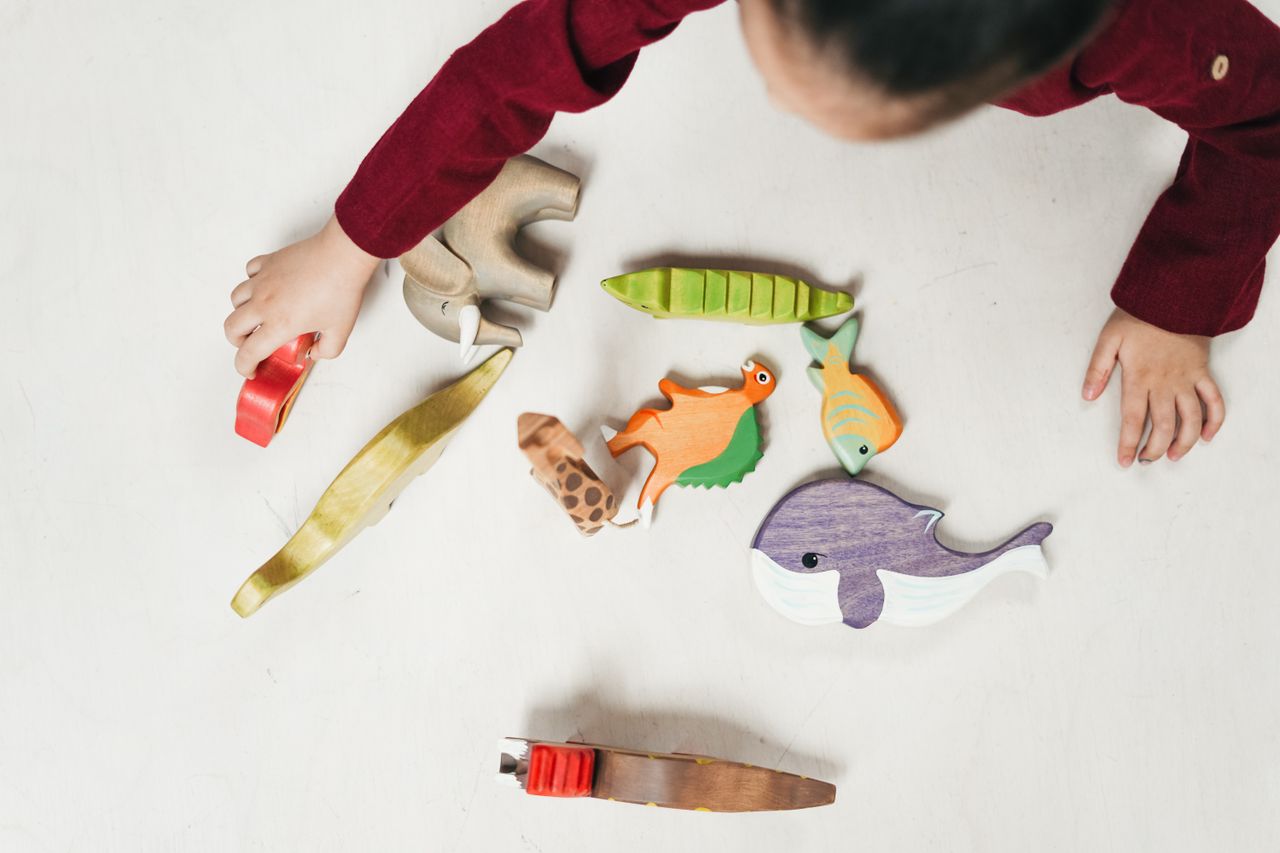 Overhead view of a child playing with colorful wooden animal toys on a white table.