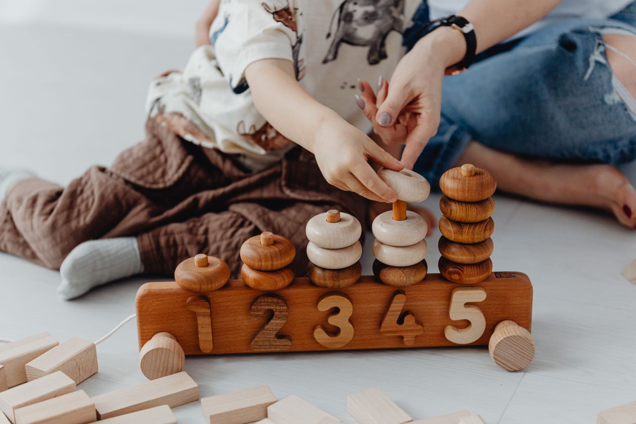 home-hero-2 A mother and child engage in playful educational activities with wooden toys, focusing on numbers.