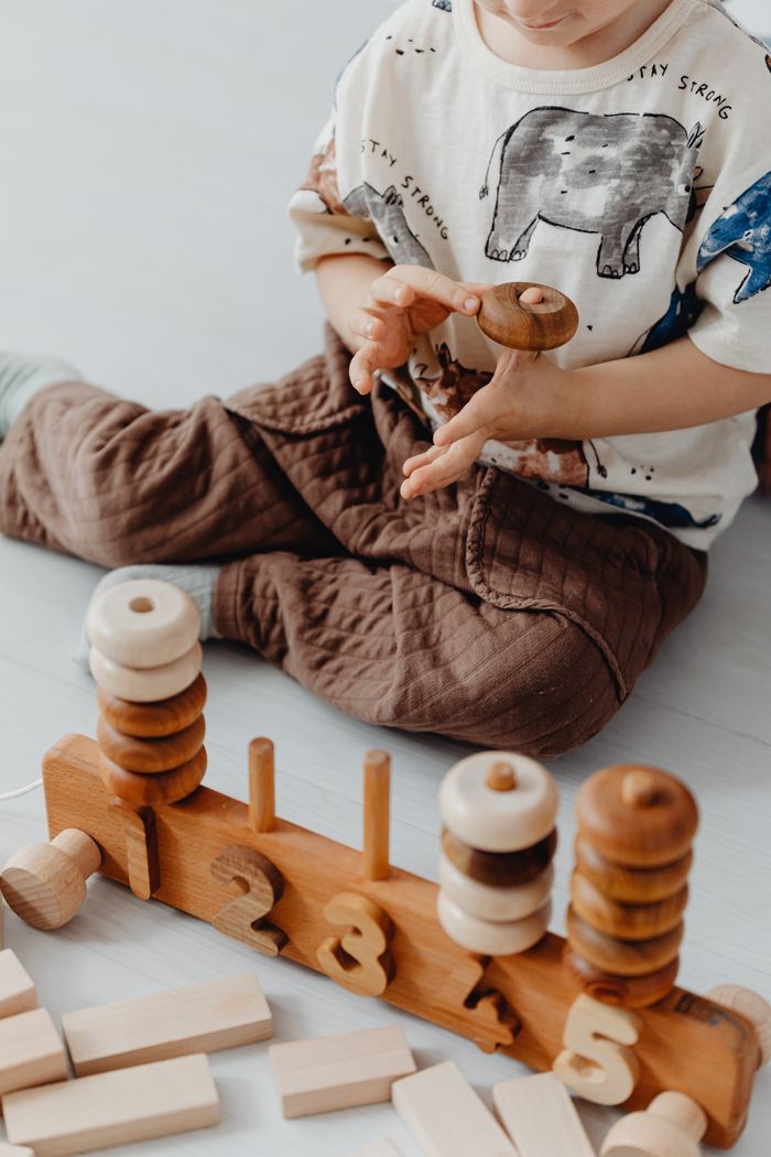 about-us-02 Young child engaged with educational wooden counting toy, enhancing motor skills and learning.