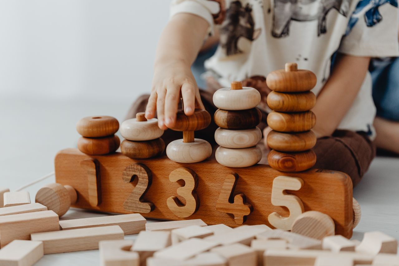 home-hero-1 Child's hand interacting with wooden educational toys and number blocks indoors.